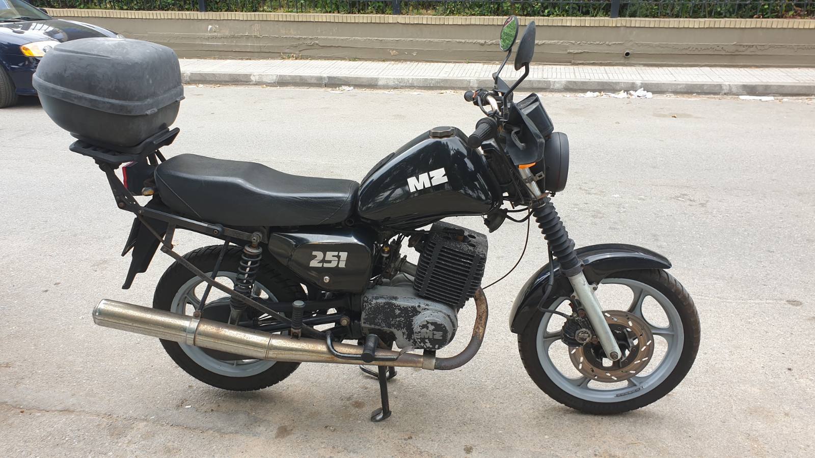 Czarna MZ ETZ 251 zaparkowana na ulicy, widok z boku – motocykl wyposażony w kufer tylni, z widocznymi śladami użytkowania na silniku i układzie wydechowym.