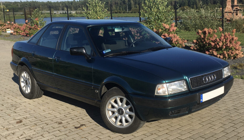 Ciemno-zielone audi 80 B4 stojące przy płocie a z tyłu jest staw