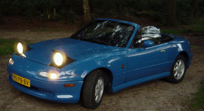 Niebieska Mazda MX-5 NA w ciemnym otoczeniu z zapalonymi światłami