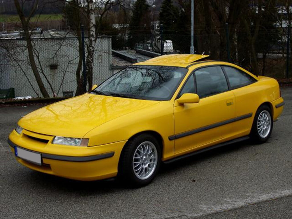 Żółty Opel Calibra zaparkowany na ulicy, ukazujący sportowy wygląd i dynamiczne linie, charakterystyczne dla samochodów lat 90.