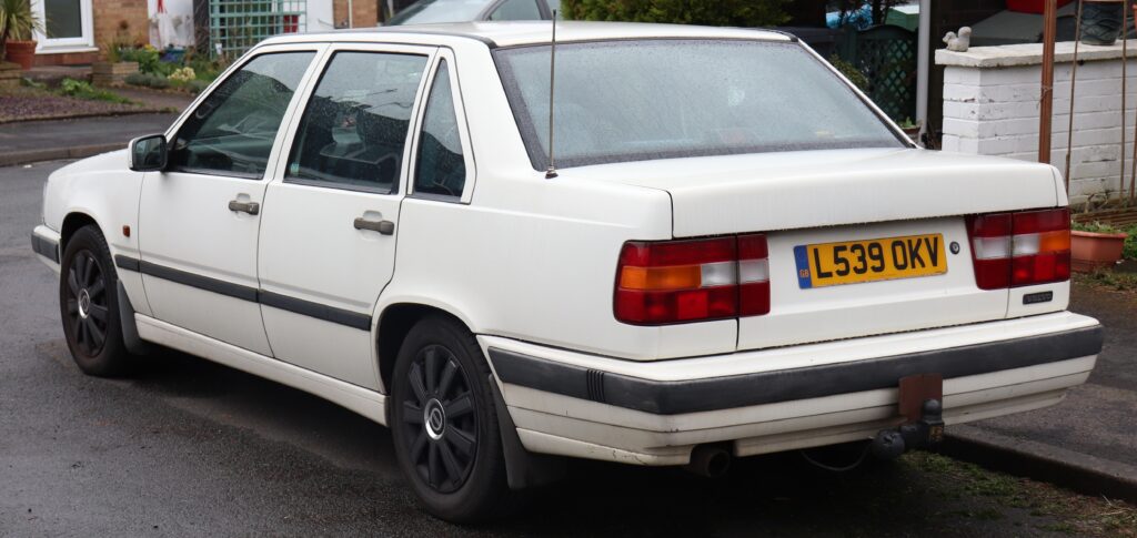 Tył Volvo 850 sedan z lat 90., biały lakier, czarne felgi i brytyjska tablica rejestracyjna