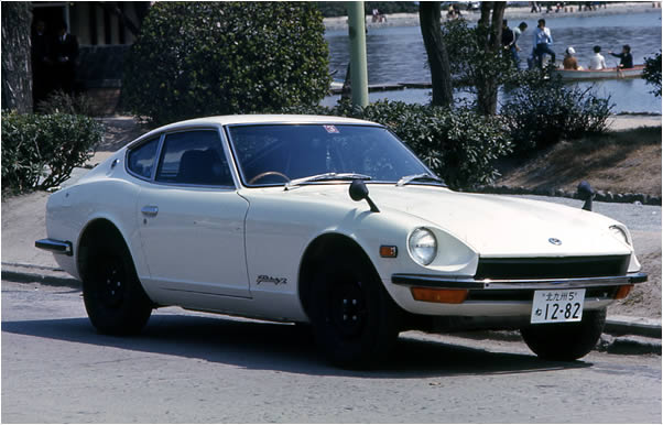 Klasyczny biały Datsun 240Z z lat 70., zaparkowany przy ulicy nad wodą – sportowy japoński fastback z charakterystycznymi reflektorami.