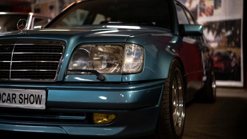 Mercedes-Benz W124 w kolorze turkusowym, wersja tuningowana z żółtymi halogenami, prezentowany na pokazie klasyków