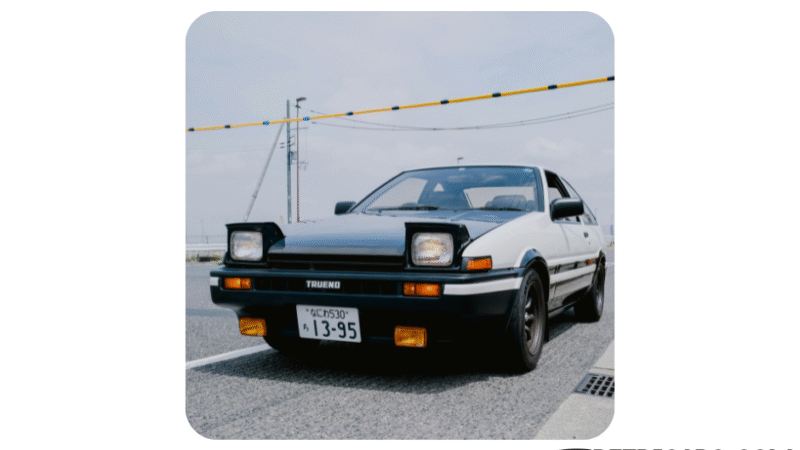 Toyota AE86 Trueno – klasyczny japoński samochód sportowy z lat 80. na grafice promującej ranking top 10 klasyków JDM sprzed 1990 roku na Retricars.com