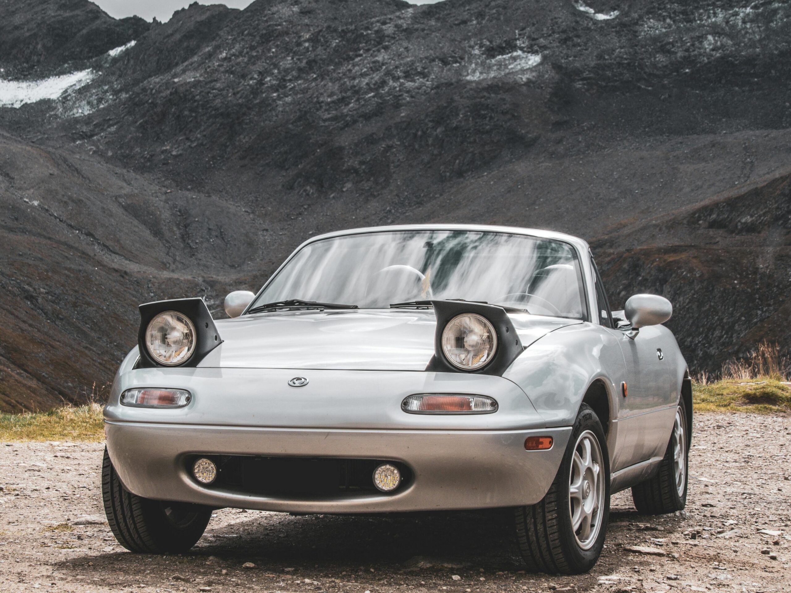 Mazda MX-5 NA z wysuwanymi reflektorami zaparkowana w górskim krajobrazie